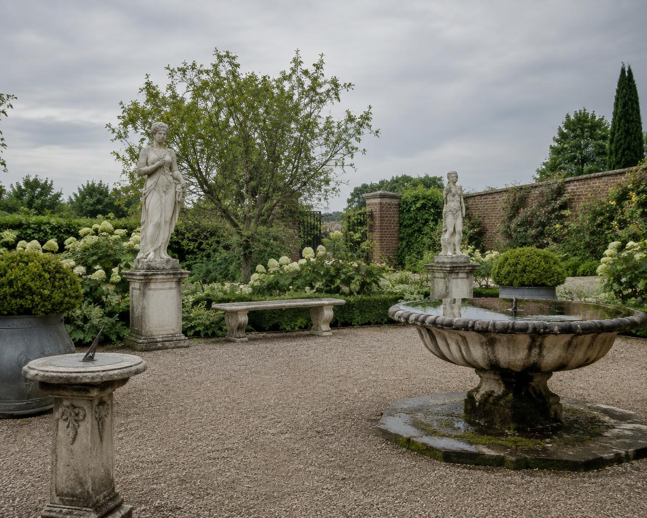 A walled garden of marble figures on plinths, a stone fountain basin, a sundial and a stone bench